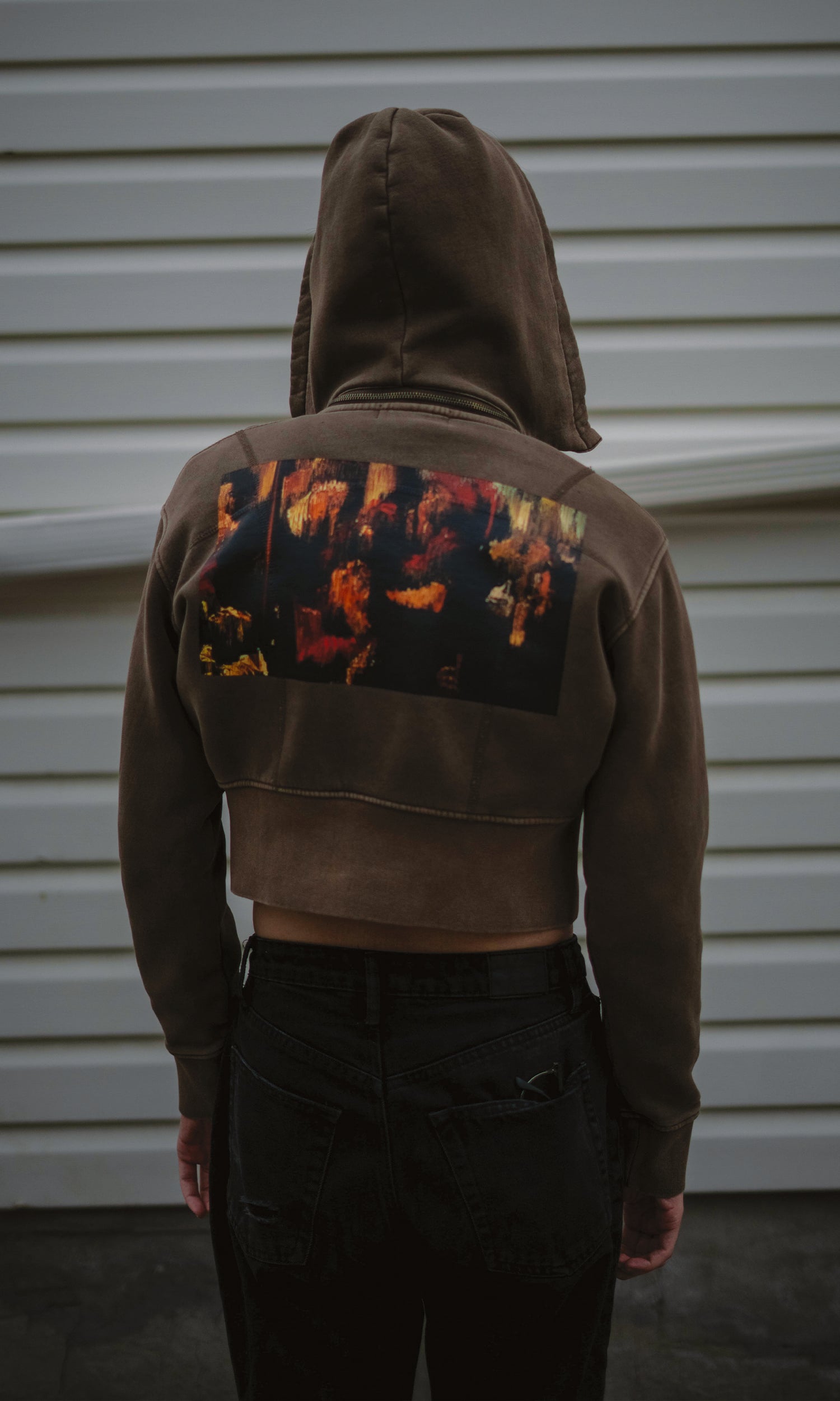 Person wearing a dark hoodie with colorful designs on the back against a light-colored wall.