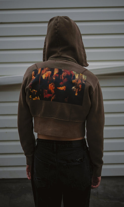 Person wearing a dark hoodie with colorful designs on the back against a light-colored wall.