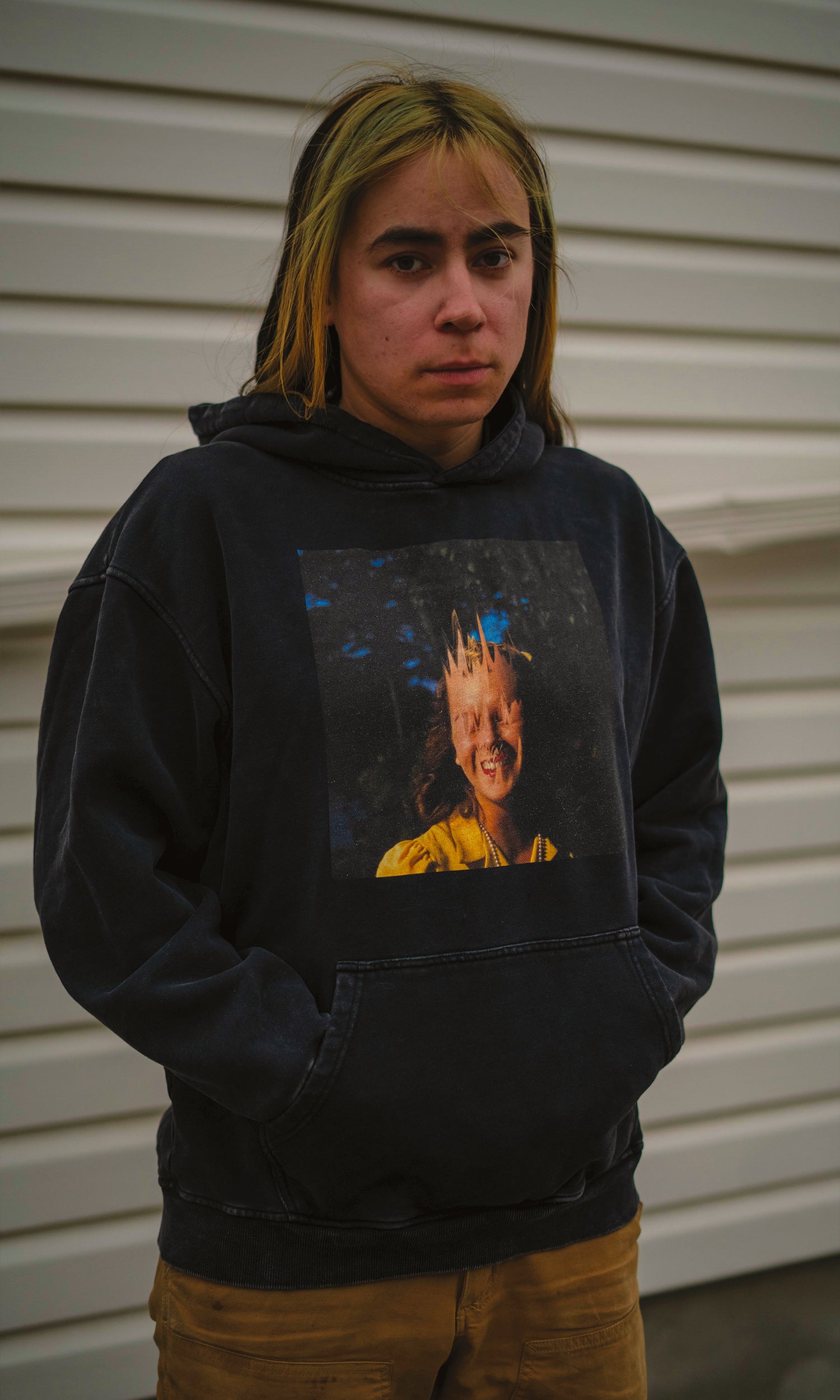 Person wearing a black hoodie with a graphic design in front of a white wall.