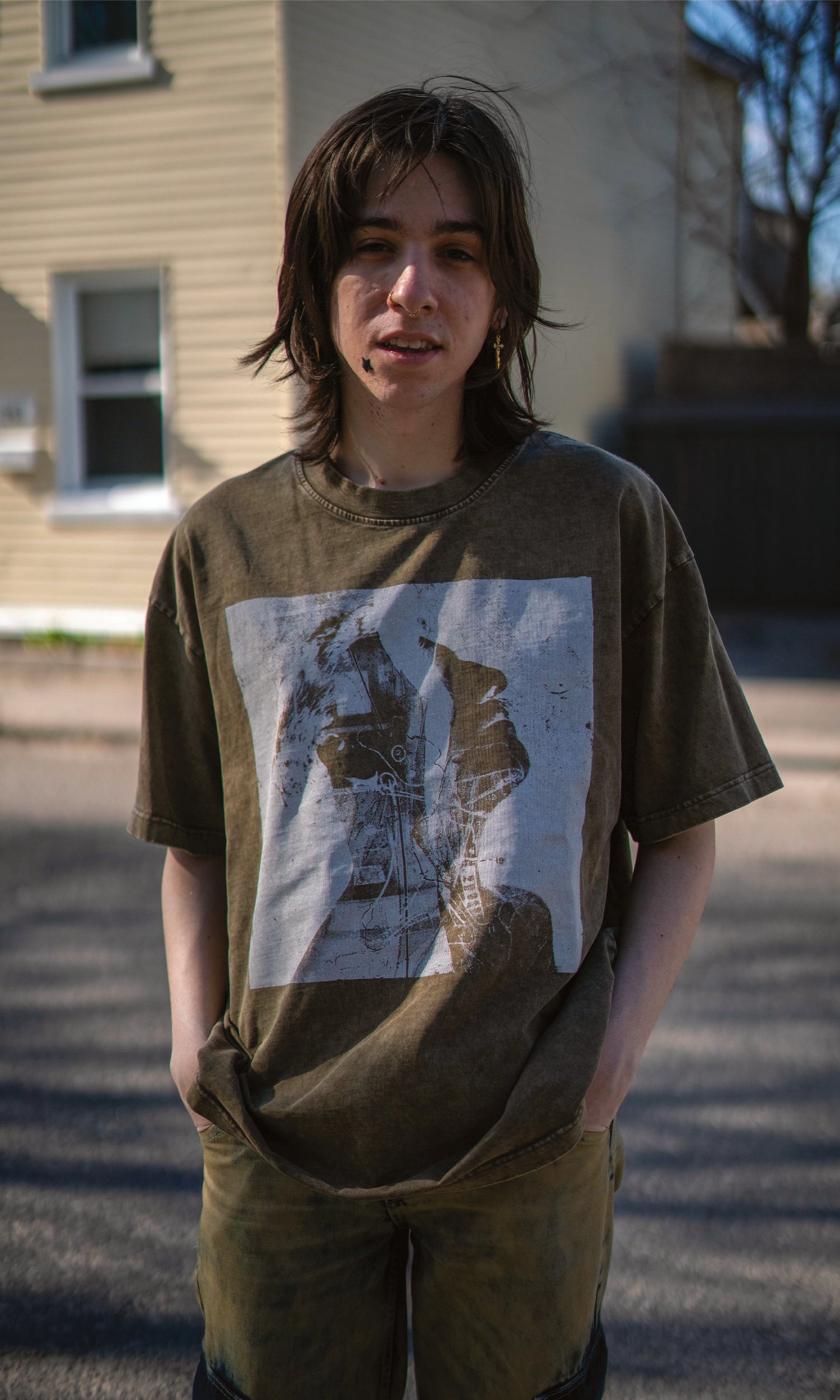 Person wearing a green t-shirt with a graphic design, standing on a street.