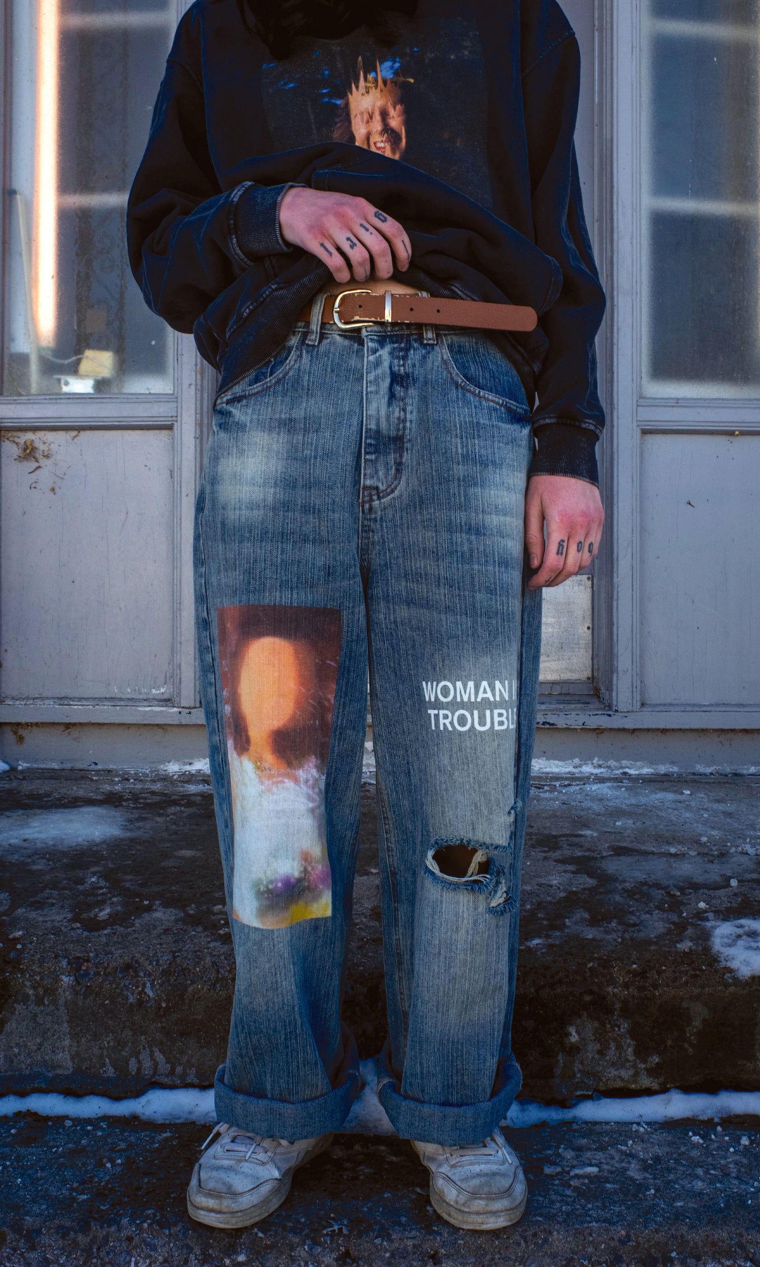 Person wearing ripped jeans with text and a graphic design, standing outdoors.