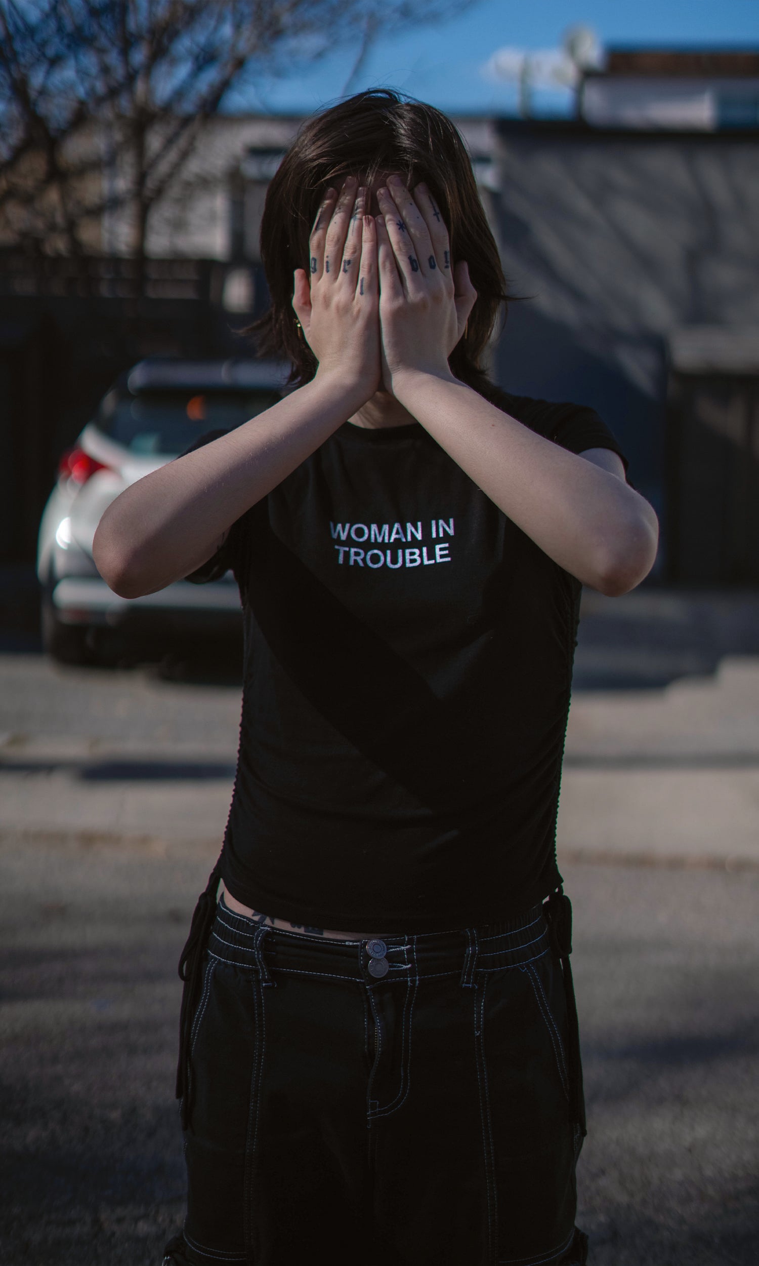 Person wearing a black t-shirt with 'WOMAN IN TROUBLE' text, standing outdoors.