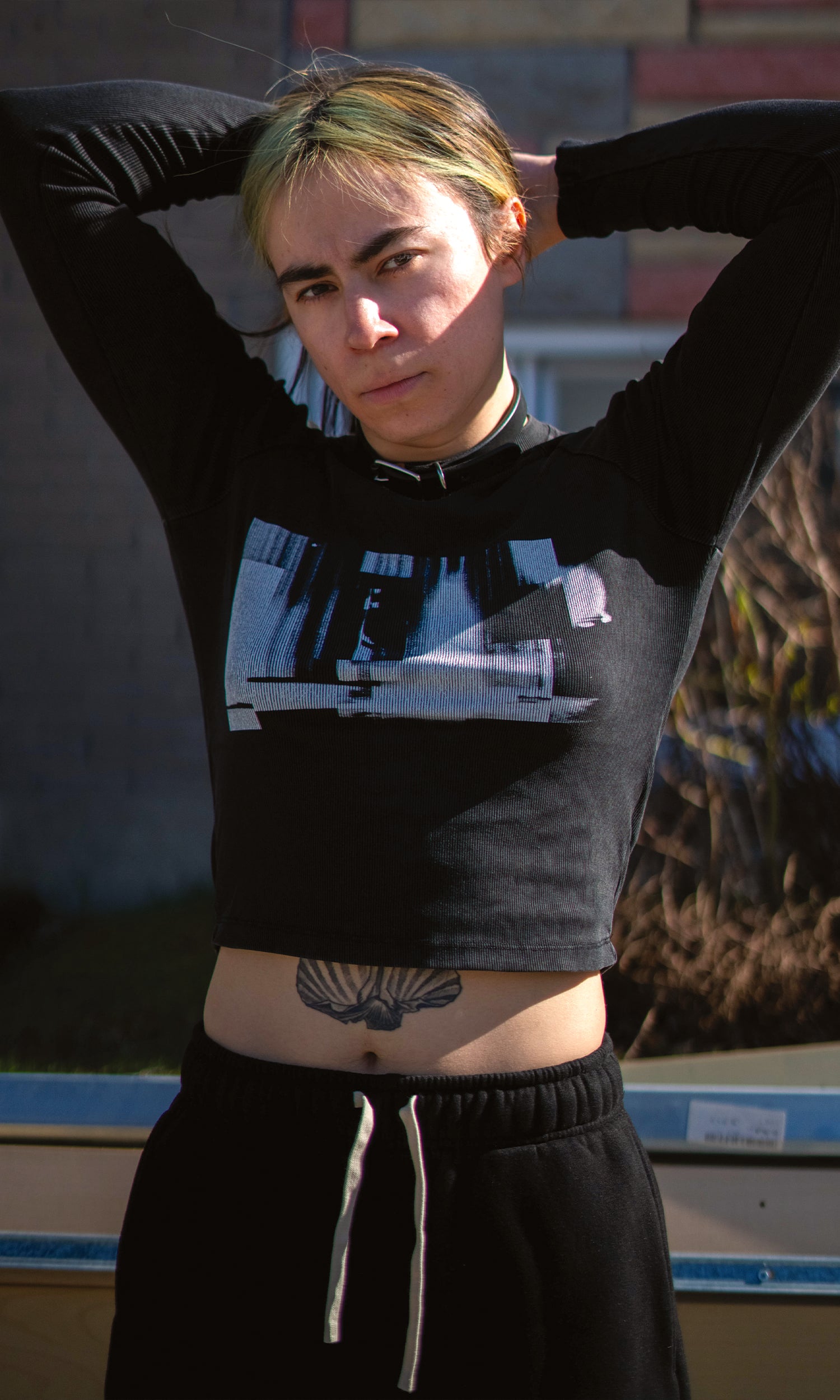 Person wearing a black and gray crop top with graphic design, standing outdoors.
