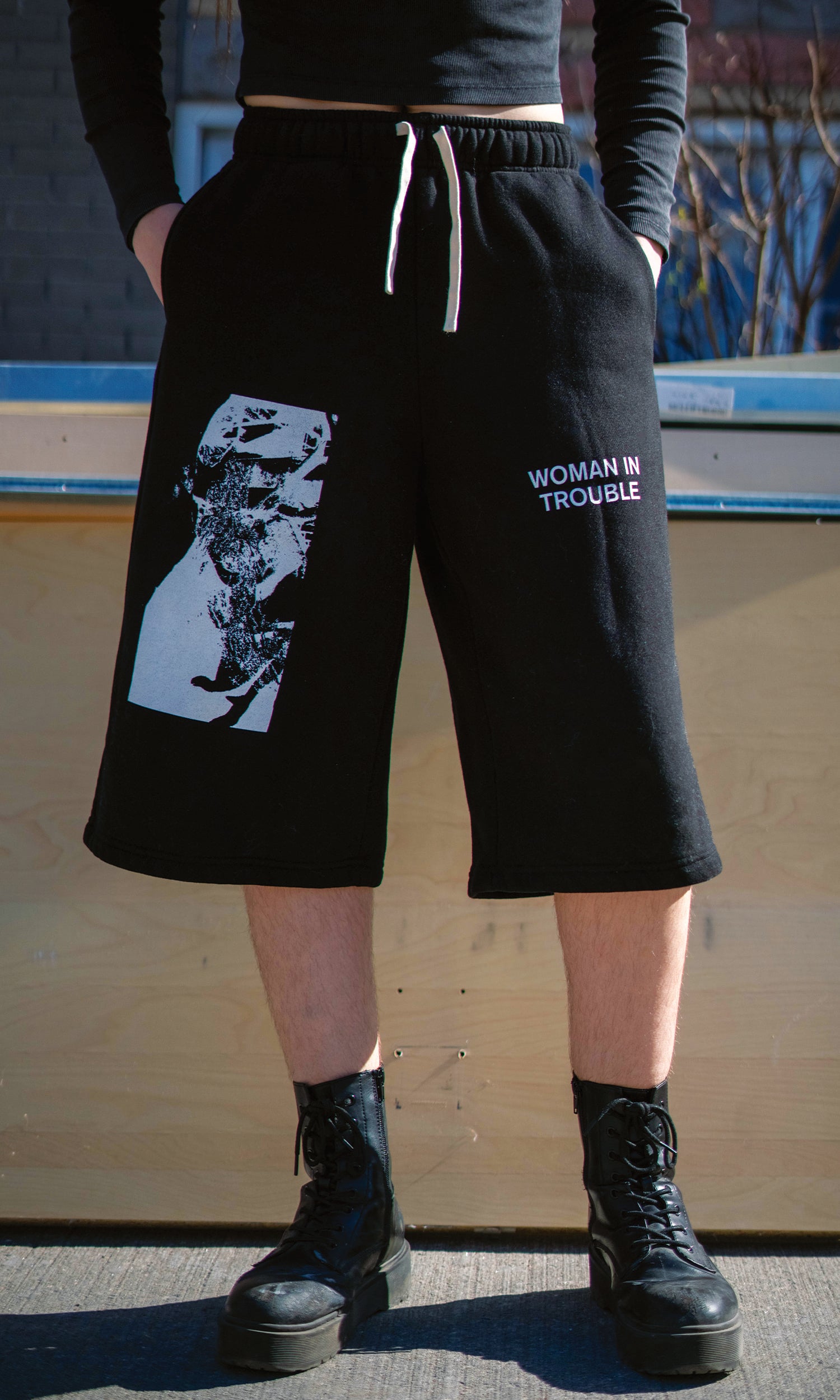 Person wearing black shorts with graphic design and text, standing against a wooden wall.
